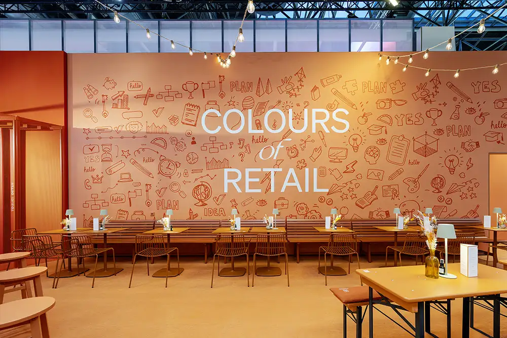 Colours of Retail creative lounge at EuroShop 2026 with collaborative seating area and illuminated retail concept wall design.